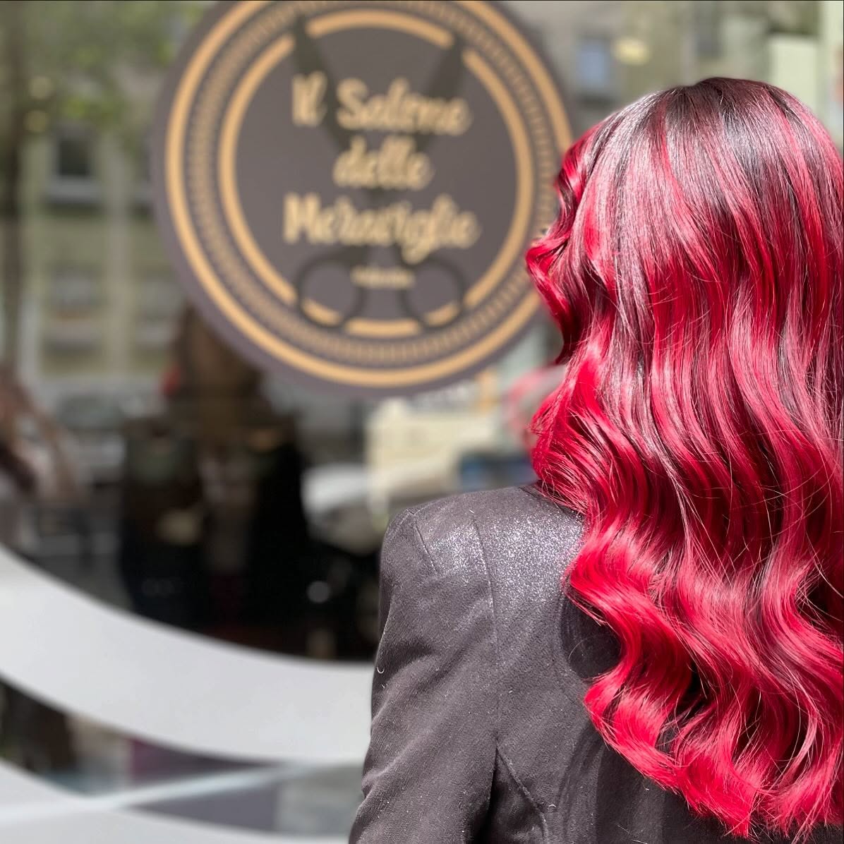 Chioma rosso intenso con onde morbide davanti alla vetrina del salone